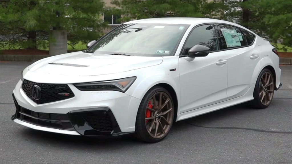 White Acura Integra Type S performance sedan parked on asphalt with bronze wheels, red brake calipers, and trees in background