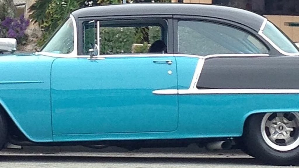 Two-tone 1955 Chevrolet Bel Air in turquoise and black, parked roadside with chrome trim and classic rounded design visible