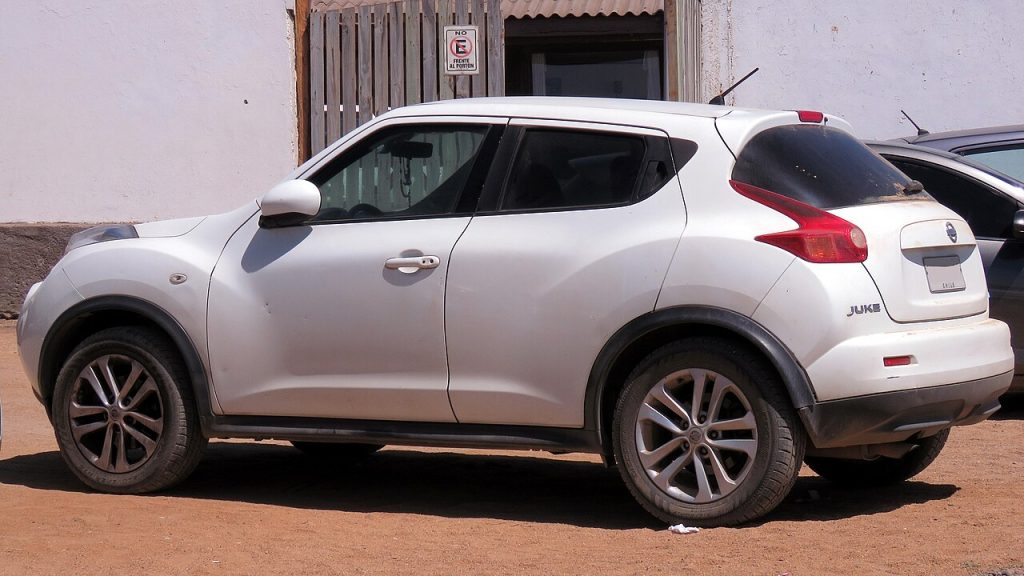 Red Nissan Juke first generation compact crossover with UK license plate RV58 LBX parked on weathered asphalt surface