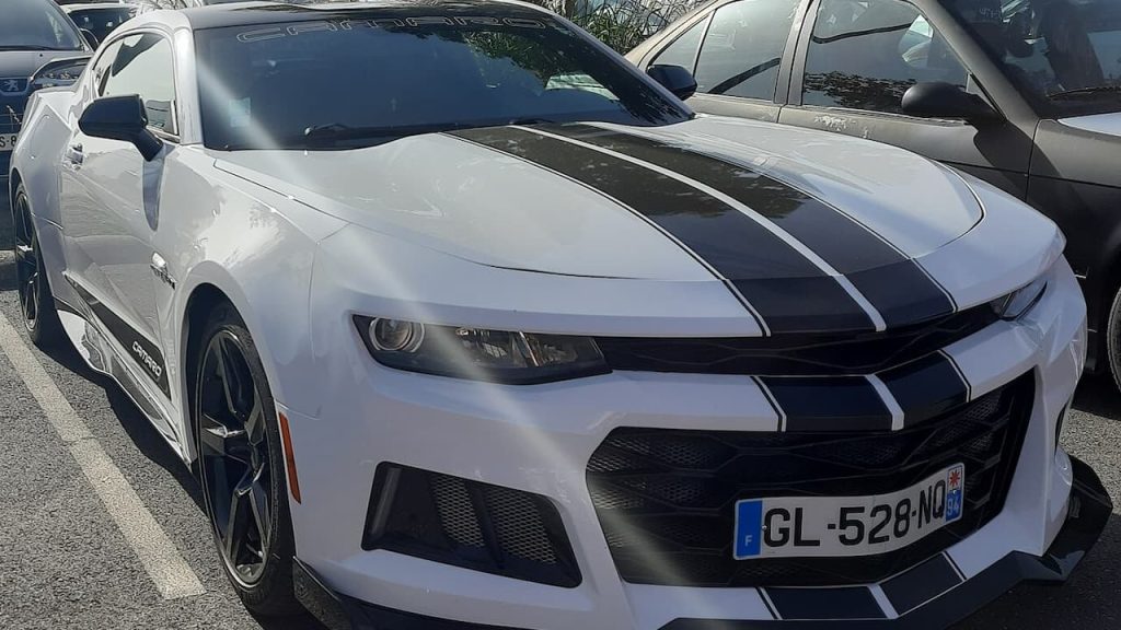 White 2023 Chevrolet Camaro ZL1 with black racing stripes parked in lot with European license plate