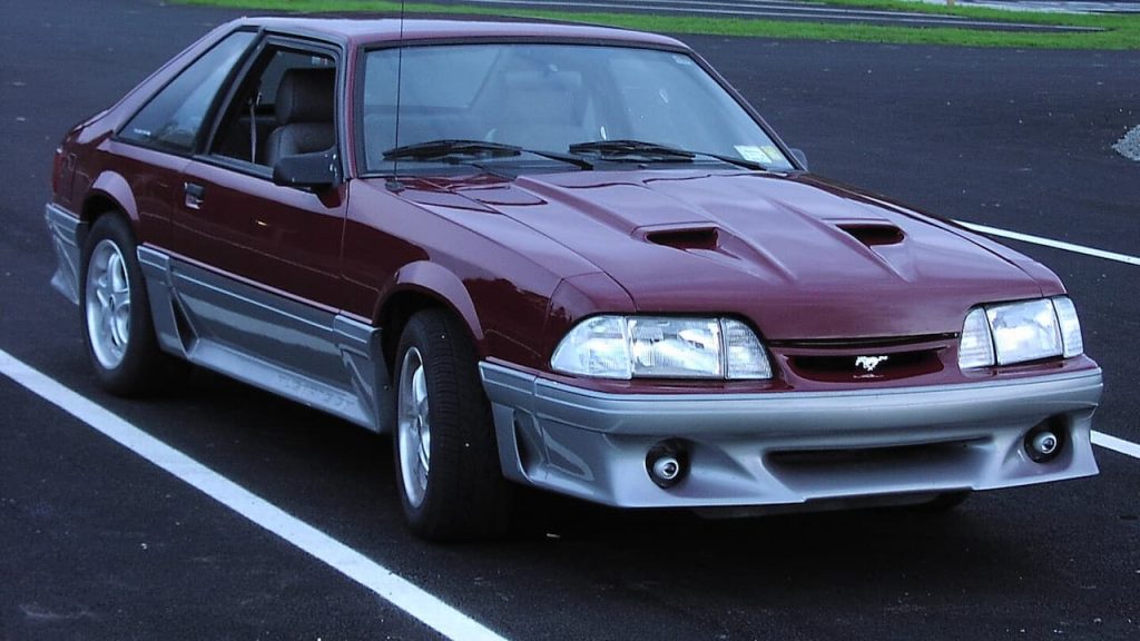 Maroon Ford Mustang GT with hood scoops and gray lower body cladding parked in marked parking space