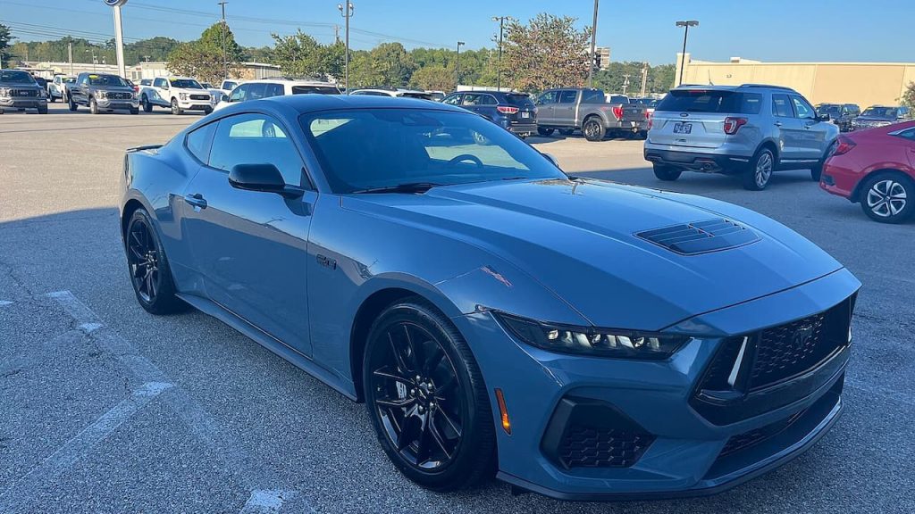 Blue 2024 Ford Mustang GT sports car parked in dealership lot surrounded by other vehicles under clear sky