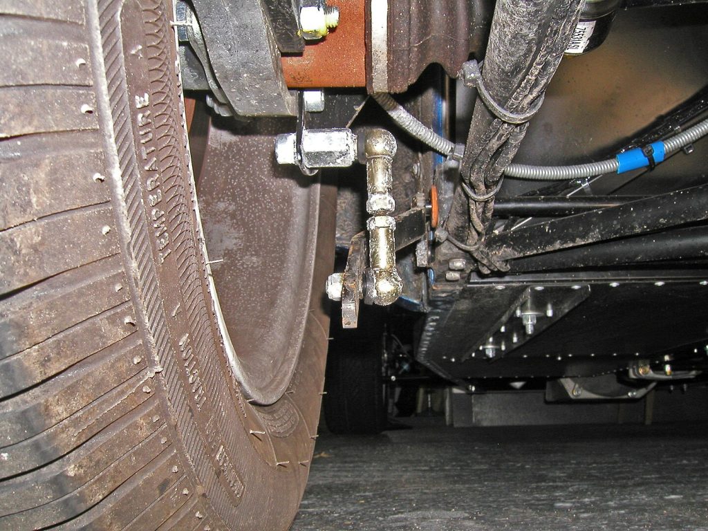 
Close-up view of vehicle's undercarriage showing tire, brake components, hydraulic lines, and mechanical parts from beneath the car