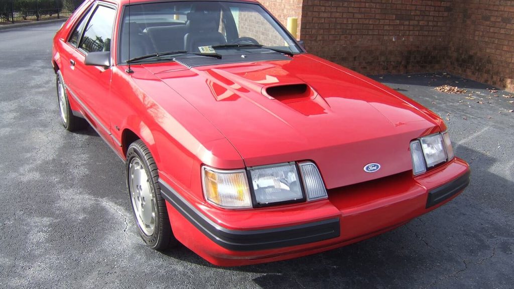 Red Ford Mustang SVO with hood scoop and distinctive front spoiler parked on asphalt near brick building