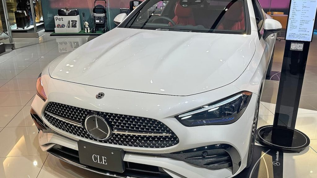  White Mercedes-Benz CLE Coupe displayed in dealership showroom with diamond grille, LED headlights, and polished tile floors