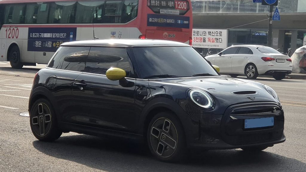 Black 2023 Mini Cooper SE electric car with yellow mirror caps parked on Korean street near bus