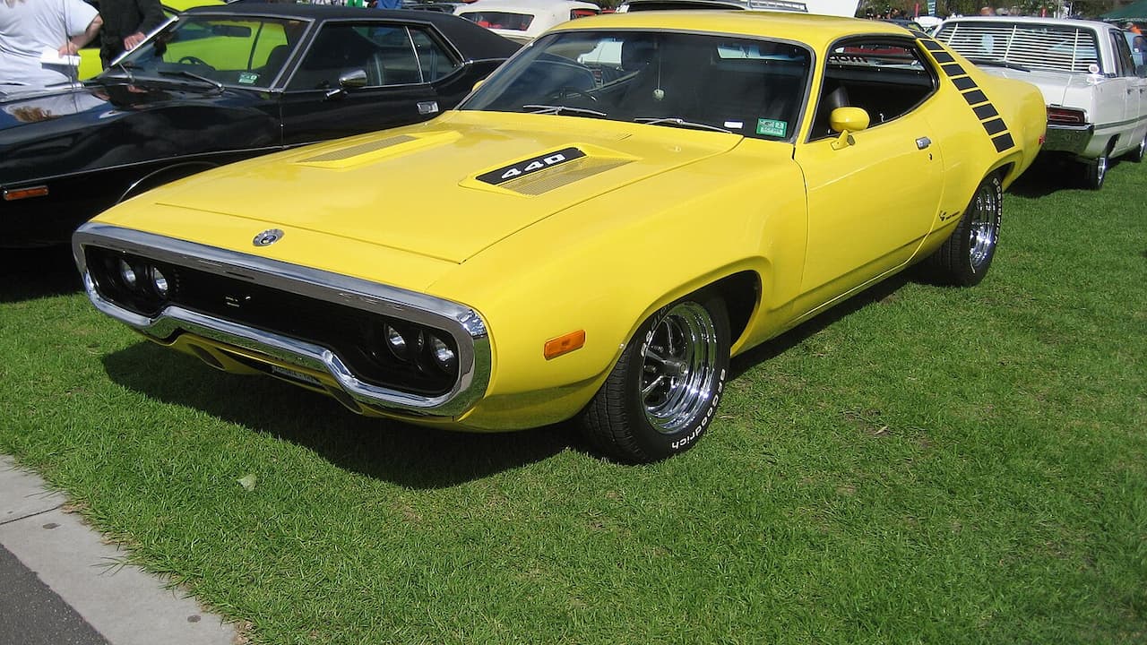 Bright yellow 1971 Plymouth Road Runner Hemi muscle car with chrome trim displayed on grass at outdoor car show