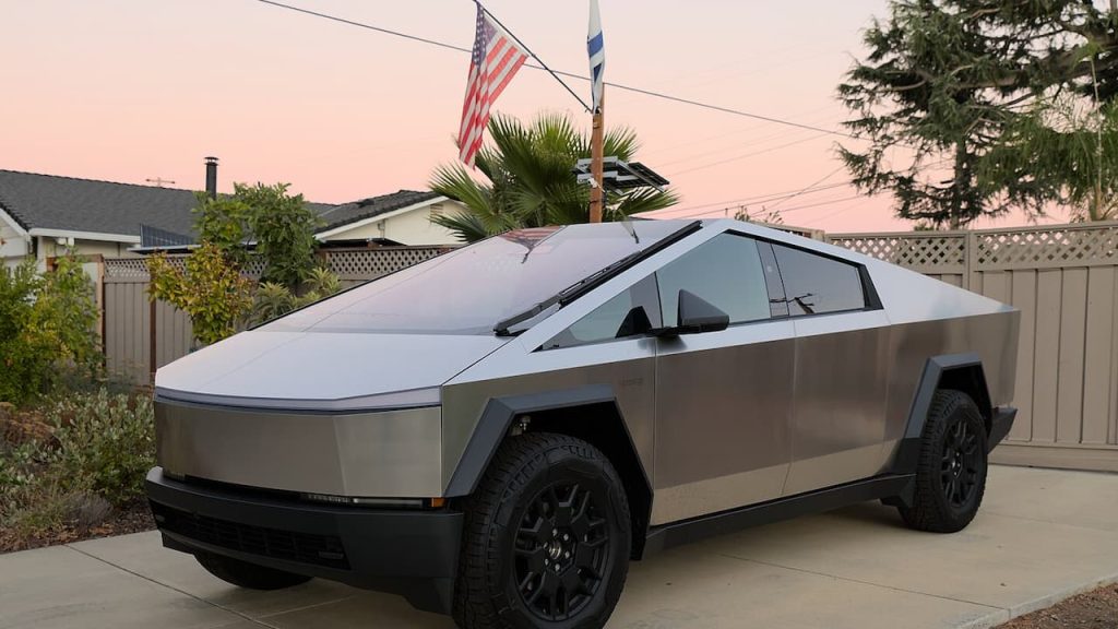 Tesla Cybertruck with angular stainless steel body parked in residential driveway with American flag and palm trees visible