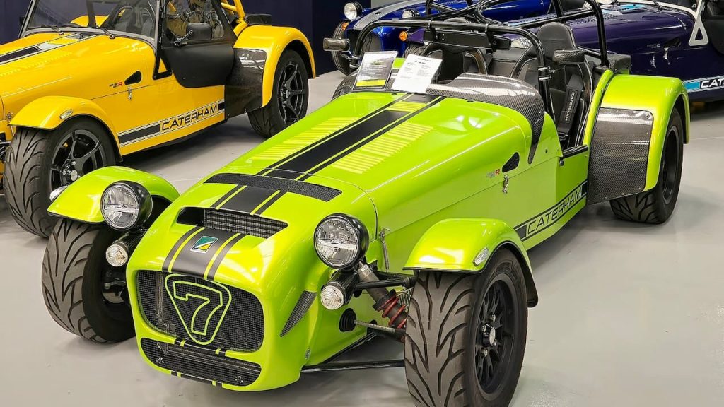 Bright green Caterham Seven 620 R lightweight sports car with black racing stripes displayed in showroom with other vehicles