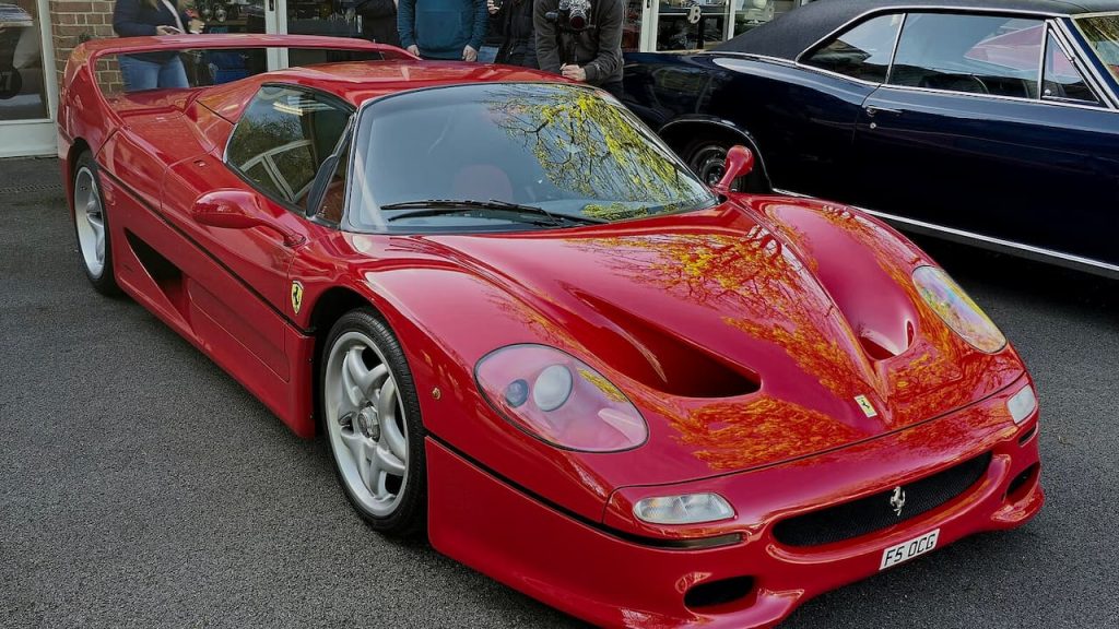  Red 1997 Ferrari F50 supercar with white wheels parked at car show with spectators and dark vehicle behind