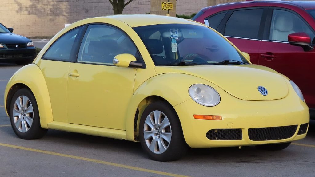 Yellow Volkswagen New Beetle parked in parking lot with round headlights, distinctive curved design, and Volkswagen badge visible