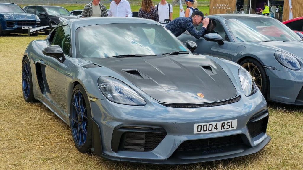  2022 Porsche 718 Cayman GT4 RS with blue wheels and racing spoiler displayed at outdoor car event