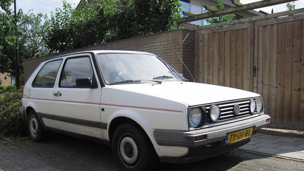 White 1989 Volkswagen Golf with Dutch license plate TY-04-BL parked in residential driveway beside wooden fence and brick wall