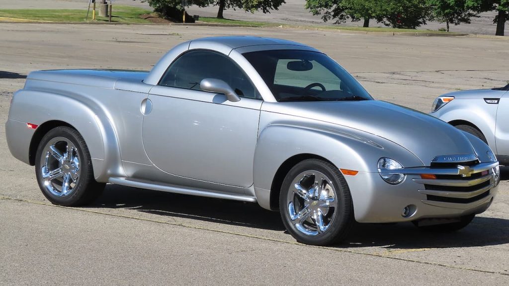 Silver Chevrolet SSR retractable hardtop pickup truck with chrome wheels parked on street with trees and buildings nearby