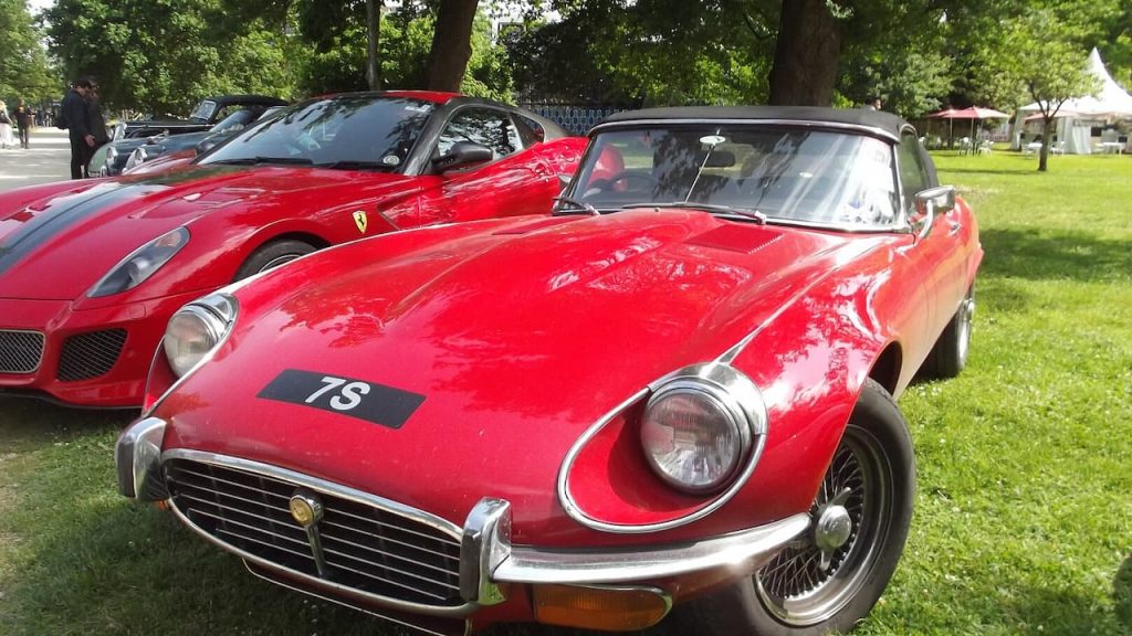 Red Jaguar E-Type V12 convertible with number 78 displayed at outdoor car show alongside other classic vehicles