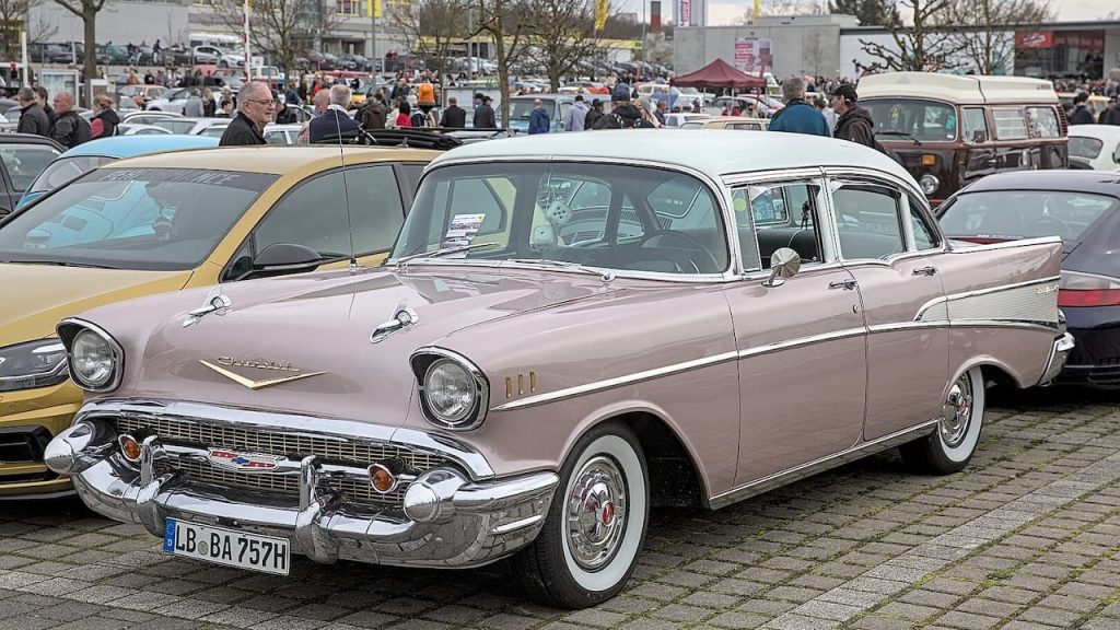 Pink 1957 Chevrolet Bel Air with whitewall tires at classic car show, surrounded by spectators and other vehicles