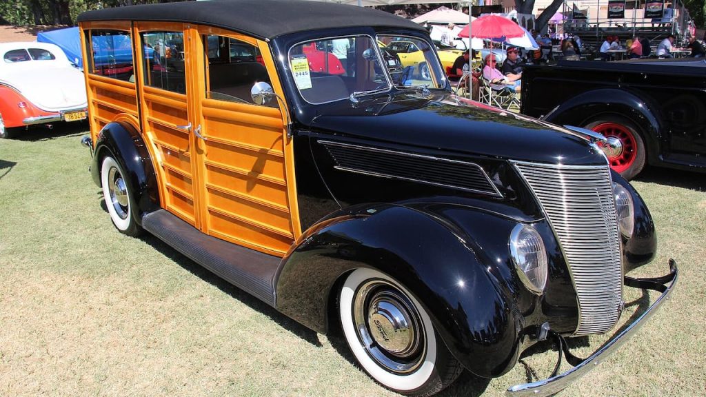 Vintage Ford woody wagon with black metal front, wooden side panels, and whitewall tires at outdoor car show