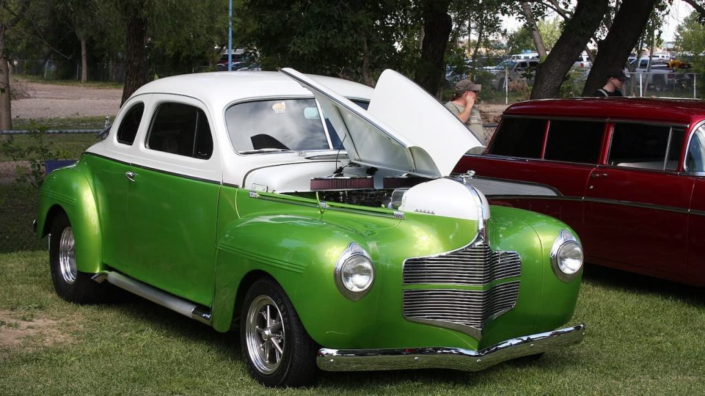 Custom two-tone 1940s Dodge coupe with metallic green lower body, white roof, open hood displaying engine at outdoor show
