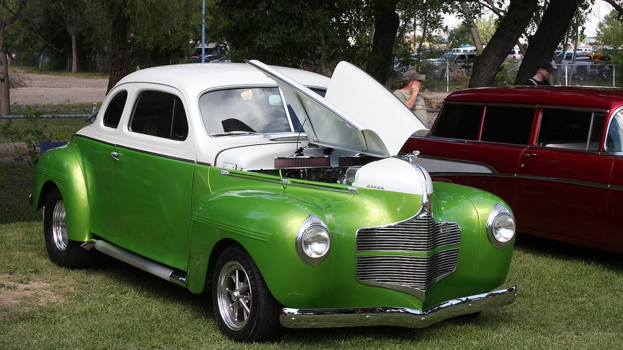 Custom two-tone 1940s Dodge coupe with metallic green lower body, white roof, open hood displaying engine at outdoor show