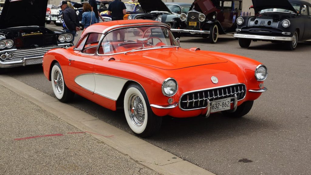 Classic red 1956 Chevrolet Corvette with white side panels and whitewall tires parked at vintage car show
