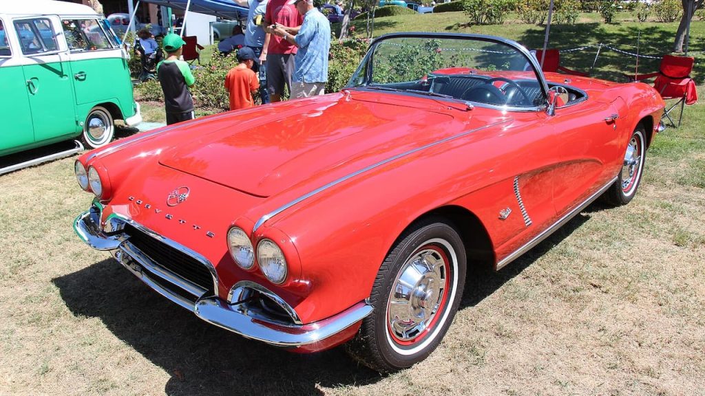 Red 1962 Chevrolet Corvette 327 V8 - 360 HP with whitewall tires and chrome details displayed at outdoor classic car show with spectators