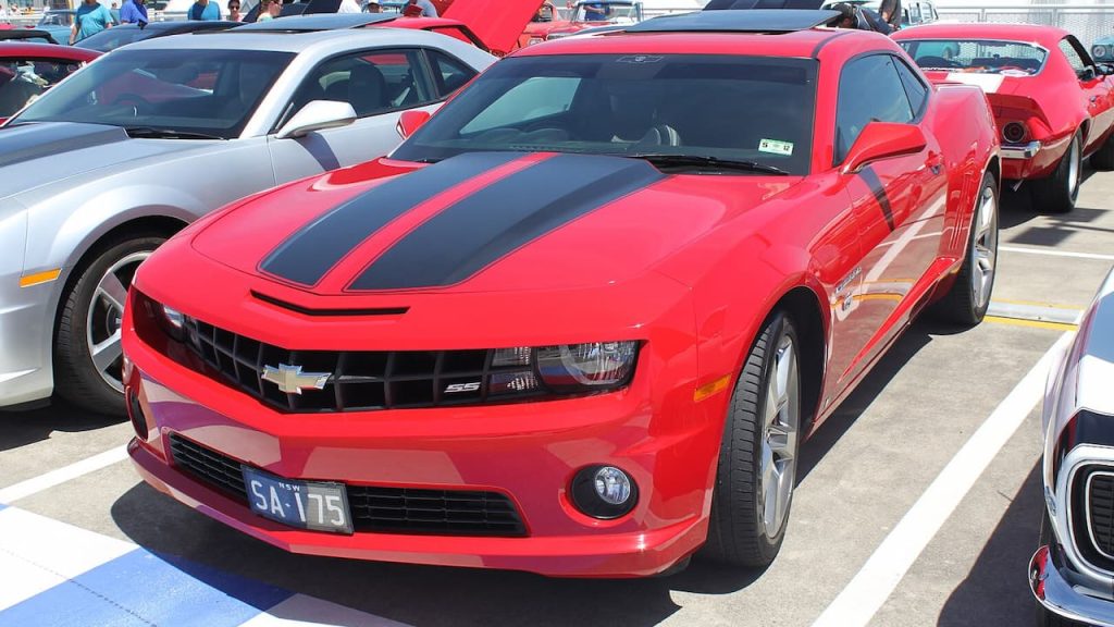 Red 2009 Chevrolet Camaro SS with black racing stripes parked at car show beside silver vehicle, license plate SA-175 visible