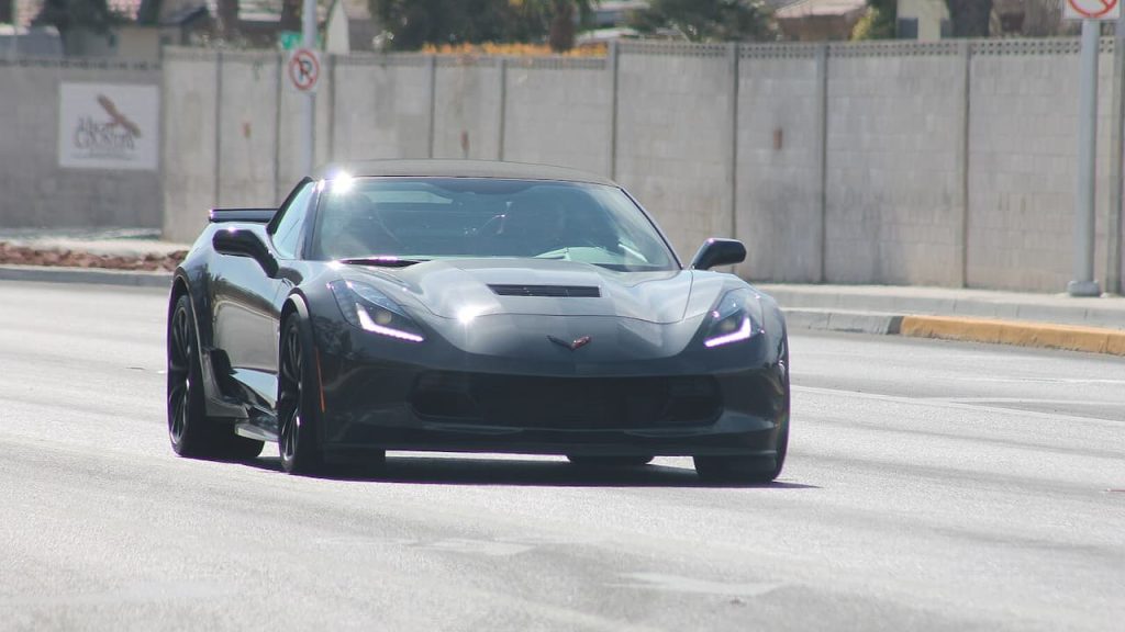 Black Chevrolet Corvette C7 Z06 with LED headlights driving on concrete road near concrete barrier wall with signage