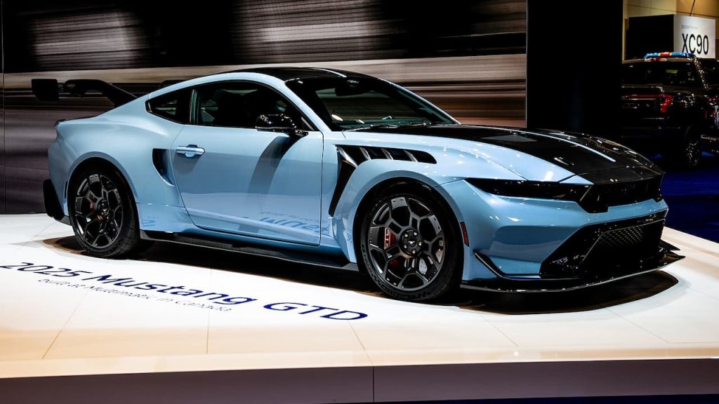 Light blue 2025 Ford Mustang GTD displayed on white platform at auto show with dramatic lighting and backdrop