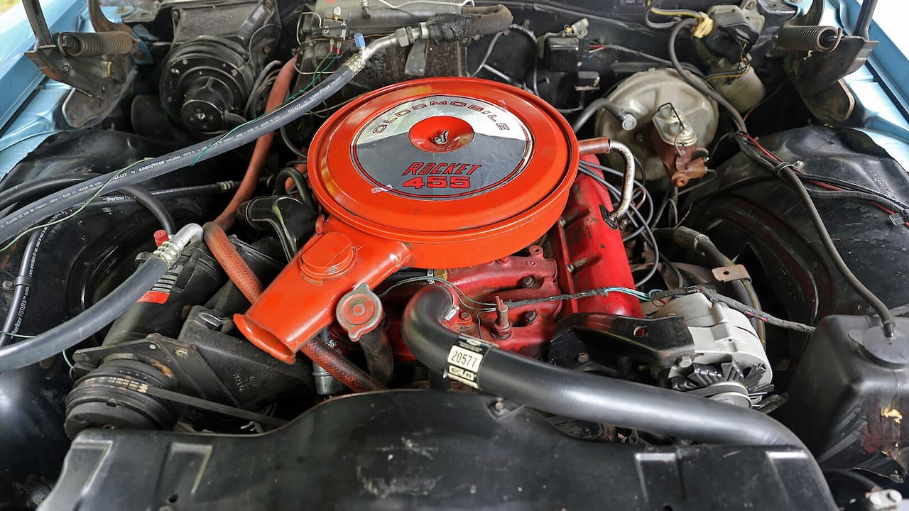 Oldsmobile Rocket 455 V8 engine with red air cleaner and valve covers, surrounded by hoses and engine components