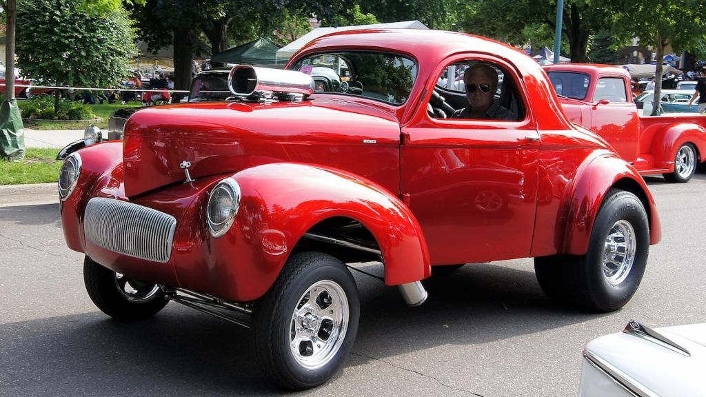 Bright red 1941 Willys Americar hot rod with chrome wheels and exposed engine scoop, driven during a classic car event