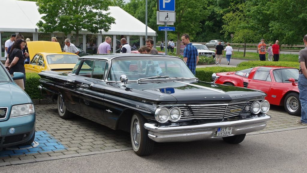 Black 1980 Pontiac Bonneville parked at classic car show with crowds, other vintage cars, and European license plate visible