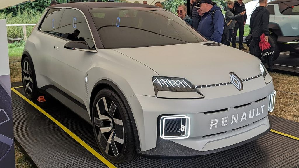 Silver Renault 5 Prototype concept car displayed on platform at outdoor event with spectators in background