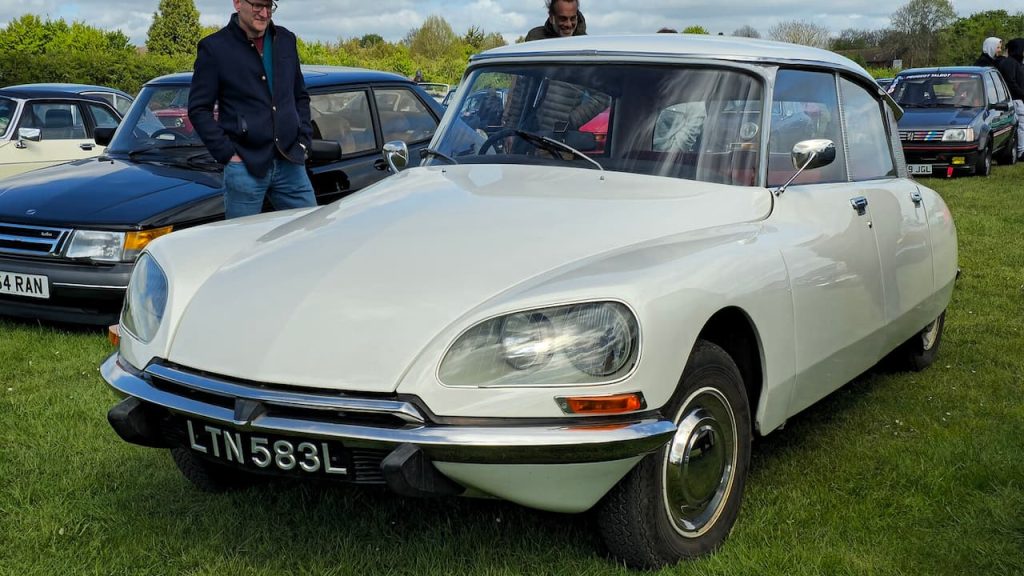 White Citroën DS classic car at outdoor car show with registration LTN583L, surrounded by other vintage vehicles and enthusiasts