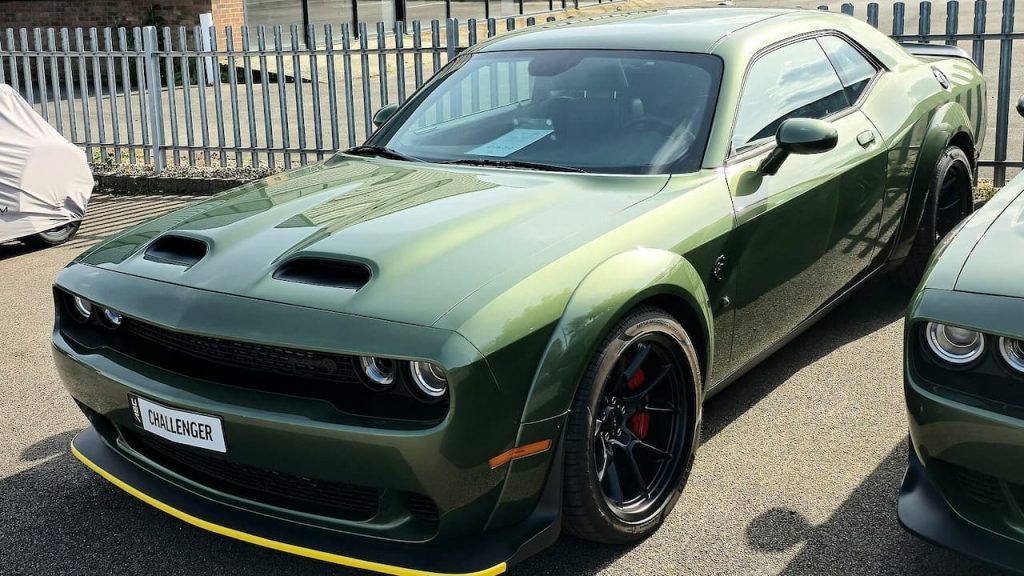 Green 2024 Dodge Challenger SRT Hellcat with dual hood scoops and black wheels parked in lot with metal fencing