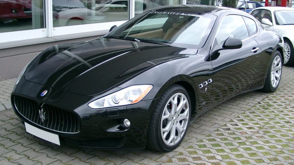 Black Maserati GranTurismo luxury coupe with distinctive vertical grille parked on cobblestone street near glass storefront