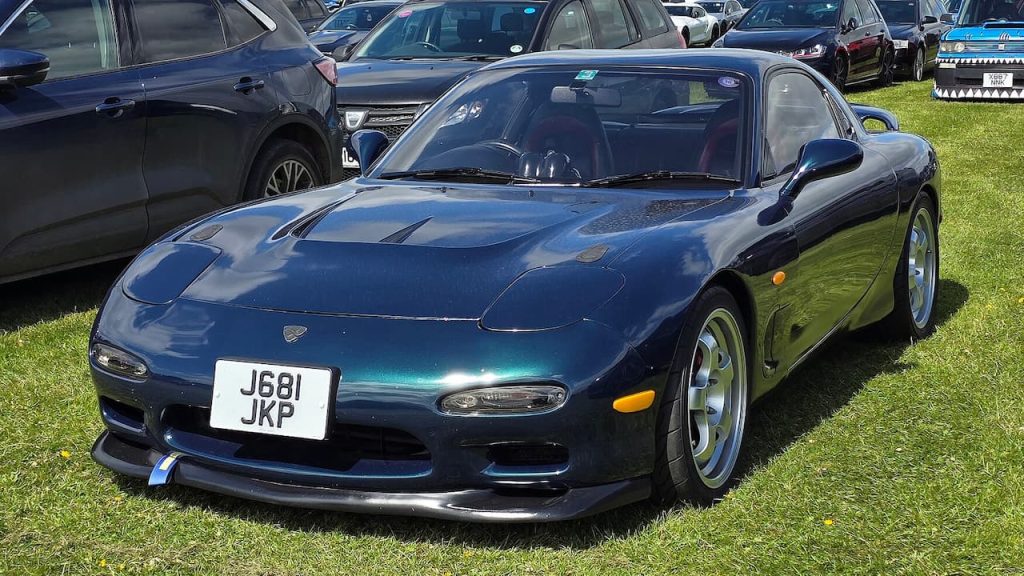 Metallic blue Mazda RX-7 sports car with license plate J681 JKP displayed on grass at outdoor car show