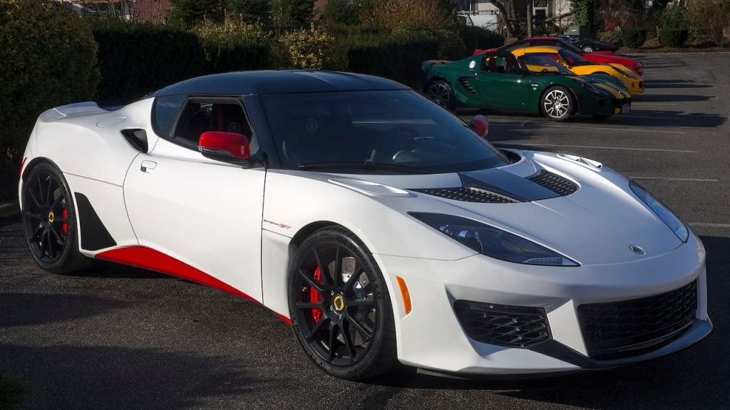 White Lotus Evora GT with red accents and black wheels parked with other colorful vehicles behind