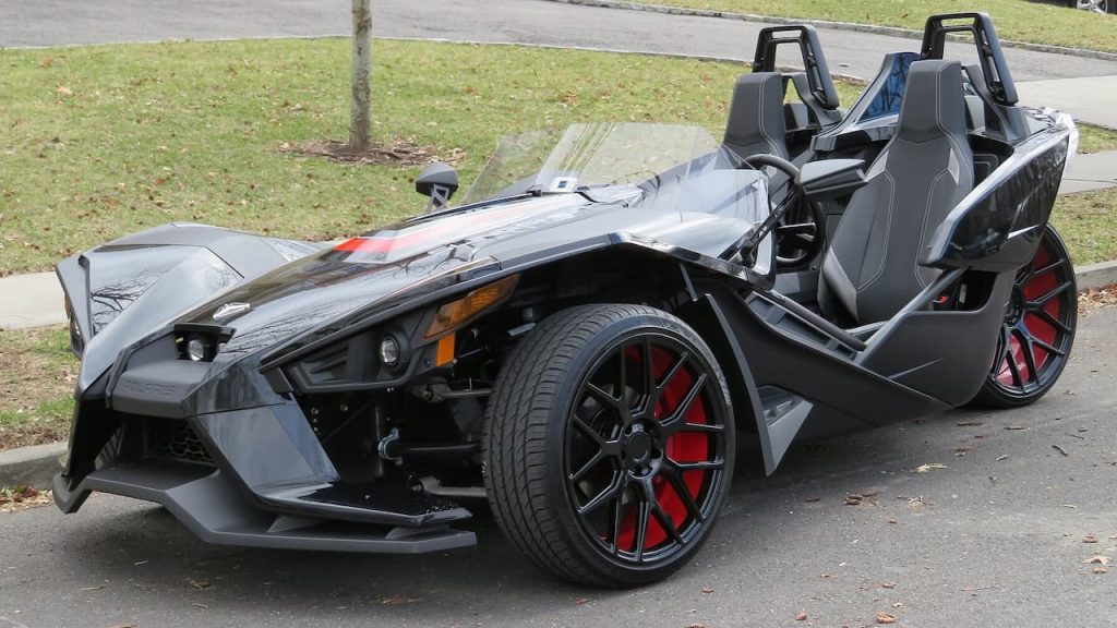 Black Polaris Slingshot three-wheeled vehicle with open cockpit, roll bars, and red brake calipers parked on residential street