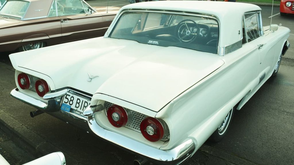 White vintage 1958 Ford Thunderbird with distinctive round taillights parked next to brown classic car in outdoor setting