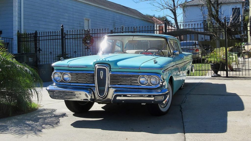 Turquoise Edsel by Ford with distinctive vertical grille and dual headlights parked on residential driveway near blue house
