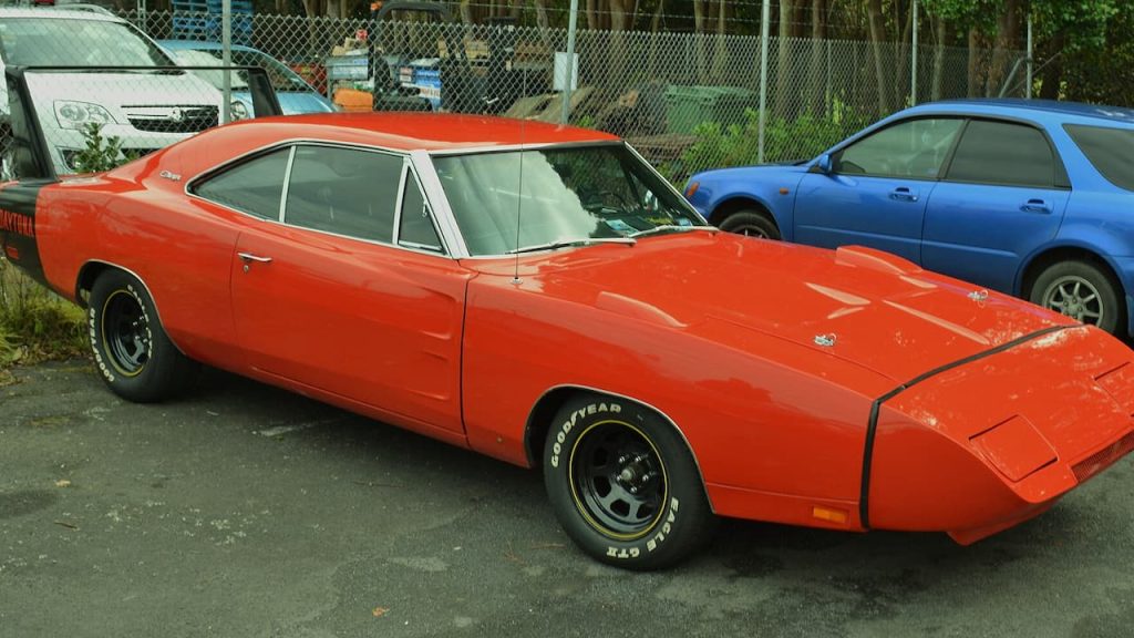 Dodge Charger Daytona with aerodynamic nose cone and Goodyear tires parked in lot beside blue sedan