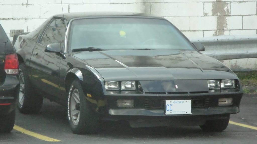 1986 Chevrolet Camaro Berlinetta with Ontario license plate parked on street near concrete block wall
