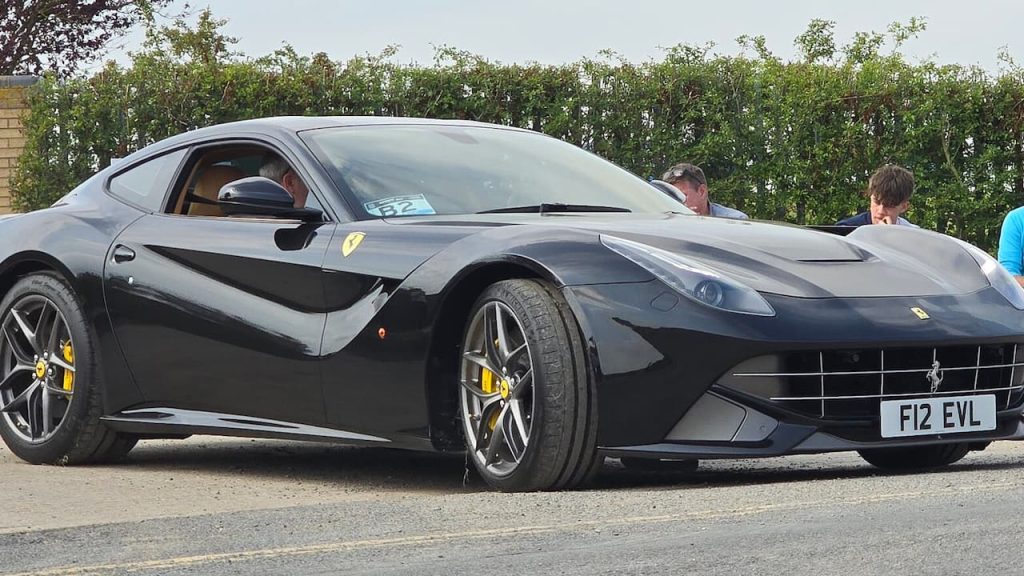 Ferrari F12 with yellow brake calipers and distinctive grille parked with onlookers nearby