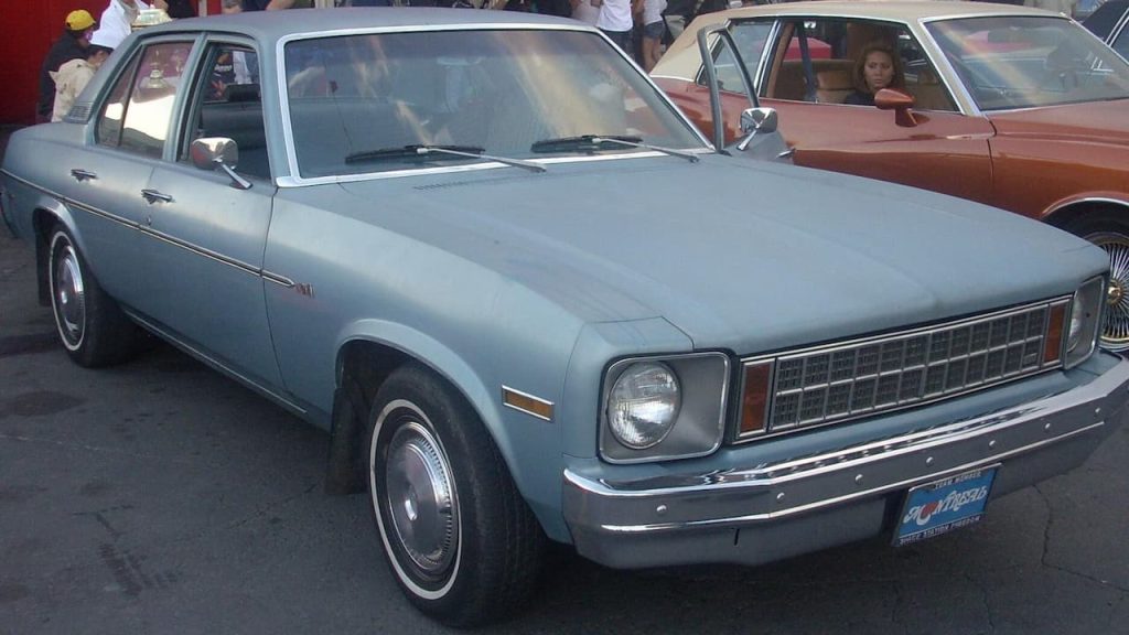 Classic Chevy Nova muscle car displayed in automotive museum showroom alongside other vintage vehicles on polished white floor