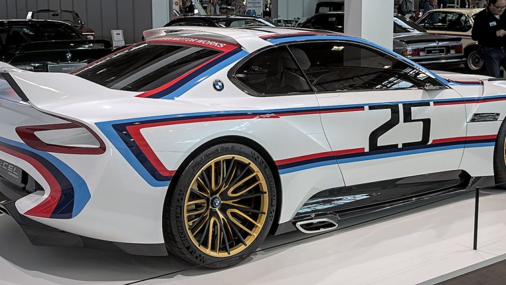 White BMW 3.0 CSL race car with number 25 and M Motorsport livery featuring gold wheels displayed at automotive exhibition