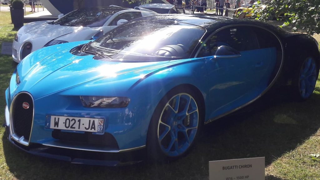 Blue Bugatti Chiron hypercar with distinctive horseshoe grille and multi-spoke wheels displayed on grass at automotive show
