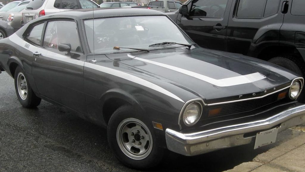Dark gray 1975 Ford Maverick Grabber with white racing stripes parked in lot surrounded by modern vehicles
