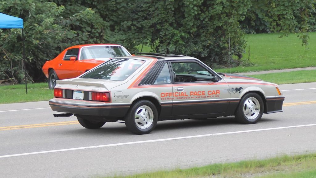 Ford Fox Body Mustang Official Pace Car with silver and orange graphics driving on road with orange Mustang behind
