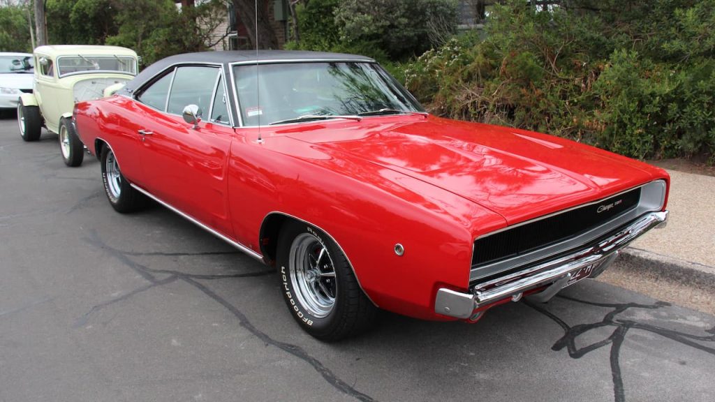 Bright red 1968 Dodge Polara 426 HEMI muscle car with black vinyl roof and chrome wheels parked on concrete with other classics