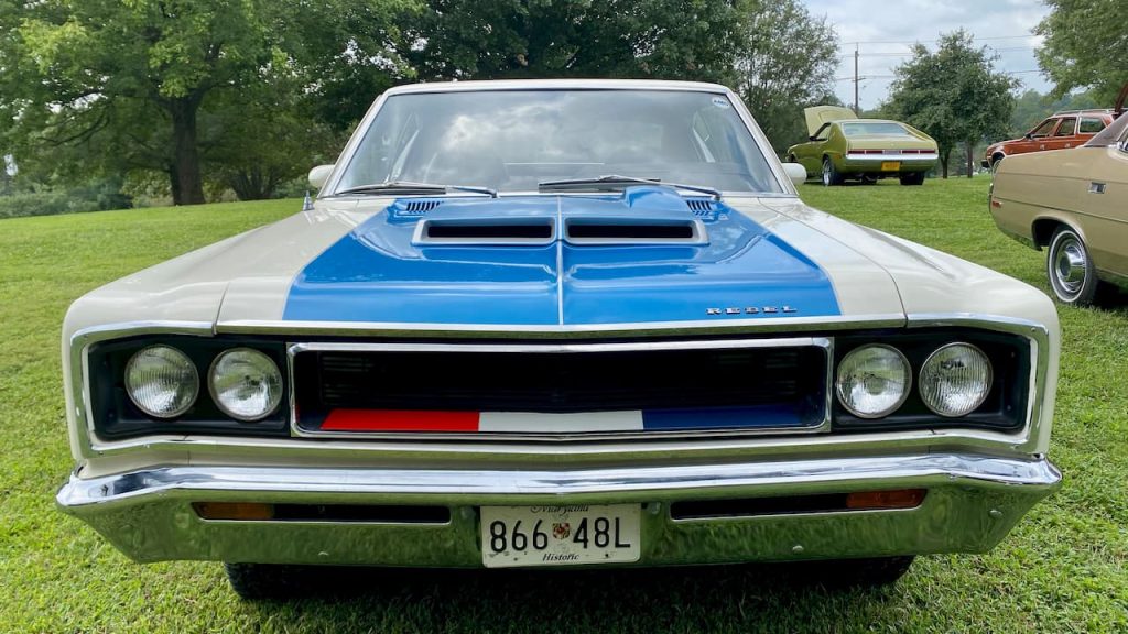 Front view of white AMC Rebel Machine with blue hood and red-white-blue grille, displayed on grass at car show